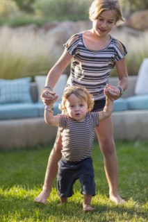 Caucasian sister helping baby brother walk in backyard