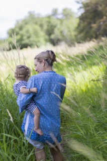 Caucasian mother carrying baby son in grassy field