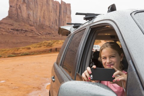 Caucasian girl taking cell phone photograph from car