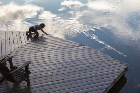 Caucasian girl on wooden deck making ripples in lake