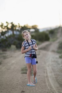 Caucasian girl carrying camera on rural dirt road