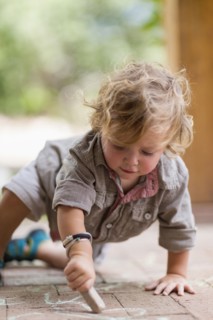 Caucasian baby boy drawing with chalk on brick patio