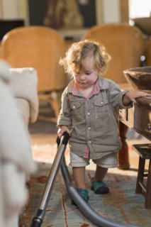 Caucasian baby boy vacuuming living room rug