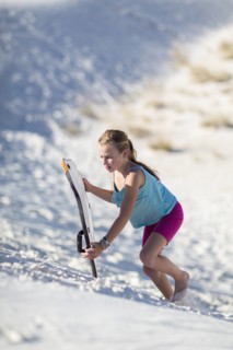Caucasian girl climbing sand dune with sled