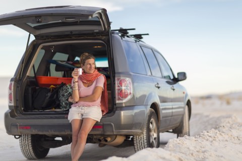Caucasian woman leaning on car drinking coffee