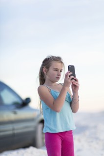 Caucasian girl taking cell phone photograph near car
