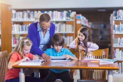 Teacher helping student use digital tablet in library