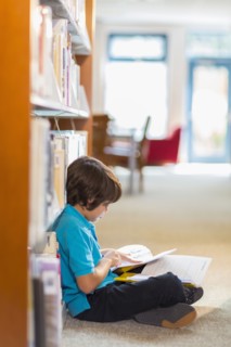 Mixed race student reading books on floor in library