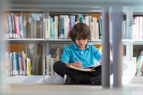 Mixed race student writing in notebook on floor in library