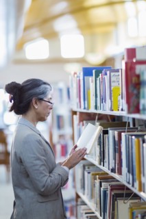 Older Hispanic woman reading book in library
