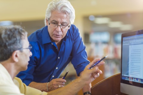 Teacher helping adult student use computer in library