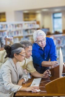 Teacher helping adult students use computer in library