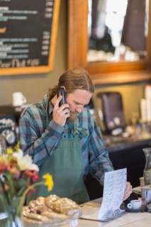 Caucasian server on telephone reading clipboard in cafe