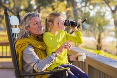Caucasian grandmother and granddaughter using binoculars on porch