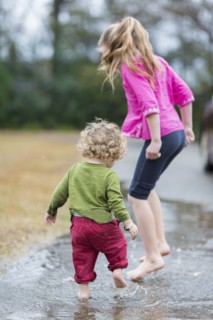 Caucasian children splashing in puddle