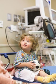 Caucasian boy sitting on hospital bed with soccer ball
