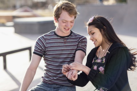 Teenage girl tying bracelet around wrist of boyfriend