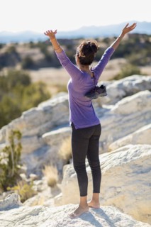Hispanic woman cheering on rocky hilltop