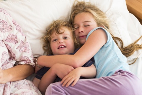 Caucasian brother and sister cuddling on bed