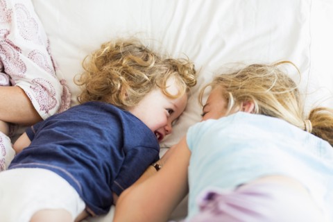Caucasian brother and sister playing on bed