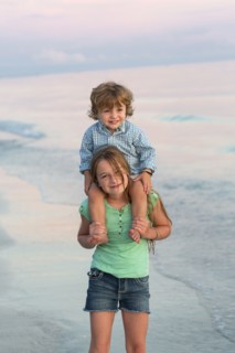 Caucasian girl carrying brother on shoulders on beach