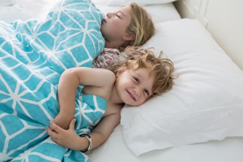 Caucasian brother and sister laying in bed