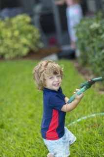 Caucasian baby boy playing with hose in backyard