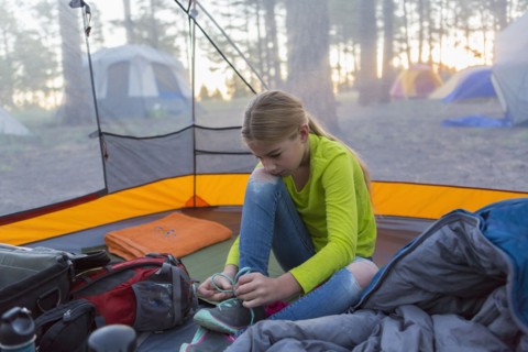 Caucasian girl tying shoes in camping tent