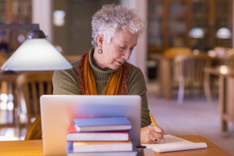 Older mixed race woman using laptop in library