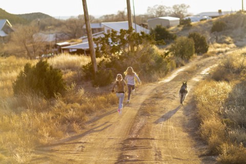 Caucasian children running on dirt road with dog