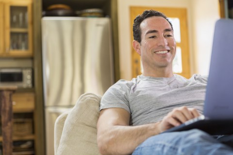 Hispanic man laying on sofa using laptop