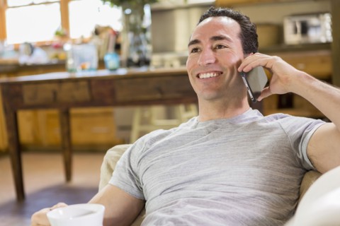Hispanic man laying on sofa using cell phone