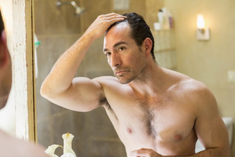 Hispanic man checking receding hairline in mirror