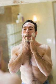 Hispanic man applying shaving cream to face in mirror