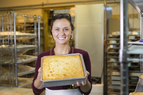 Caucasian woman showing cake in bakery pan