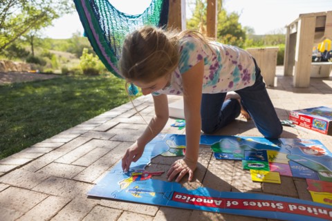 Caucasian girl kneeling on patio assembling puzzle