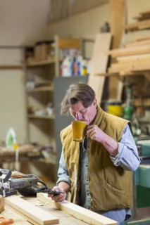 Caucasian carpenter drinking coffee and texting on cell phone in workshop