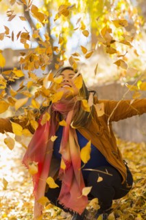 Smiling Asian woman throwing leaves in autumn