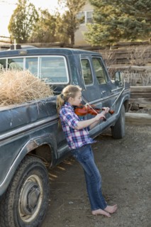 Caucasian girl leaning on truck playing violin
