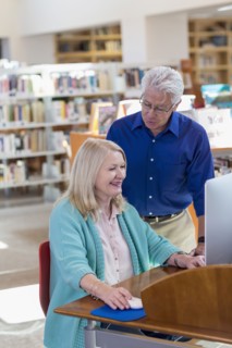 Older man watching woman using computer in library
