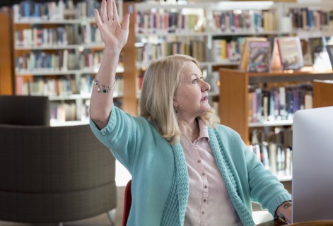 Caucasian woman using computer in library raising hand