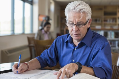 Hispanic man reading book and writing notes in library