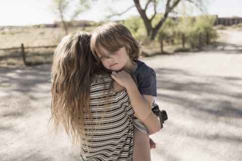Caucasian girl carrying brother on dirt path
