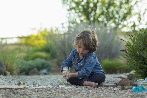 Caucasian boy sitting on ground smashing rocks with hammer
