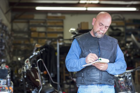 Caucasian man near motorcycle writing on notepad