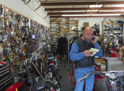 Caucasian man holding notepad near motorcycle talking on cell phone