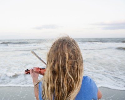 Rear view of Caucasian girl playing violin at beach