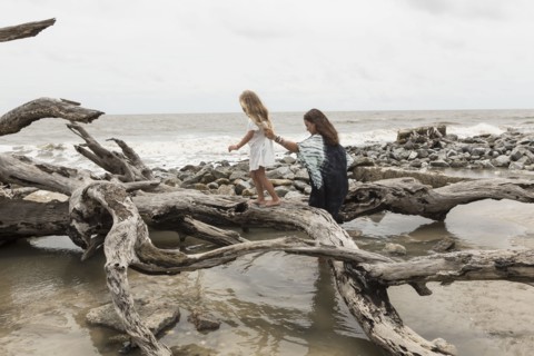 Caucasian mother and daughter walking on driftwood on beach