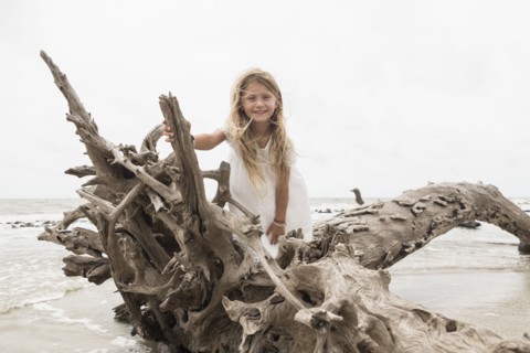 Caucasian girl posing on driftwood on beach