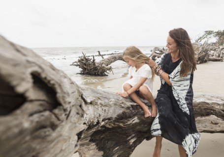 Caucasian mother and daughter sitting on driftwood on beach
